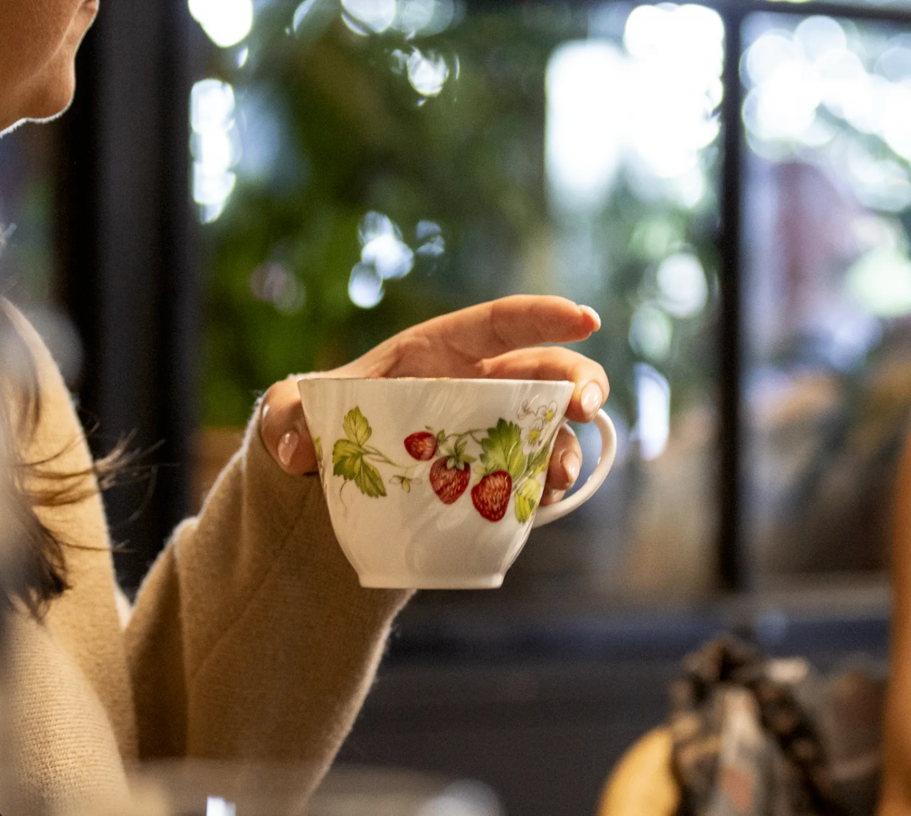 Close-up of a member holding a vintage strawberry teacup at a Circle gathering
